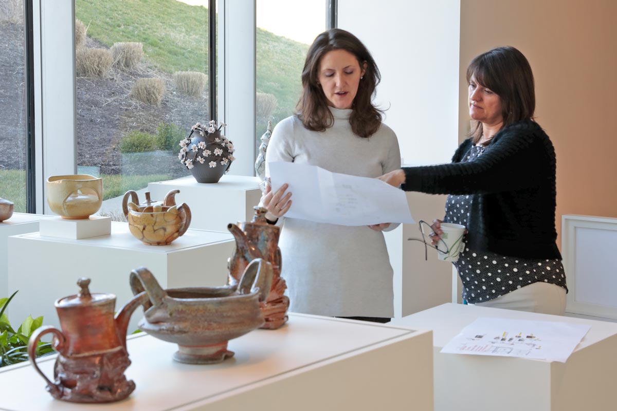 Dena Rigby working on art installation for the Workhouse Resident Artists with Anne Fletcher, Art Administrator for Capital One, featuring artwork by Brian Grow and Joan Ulrich; photo by David Hunter Hale
